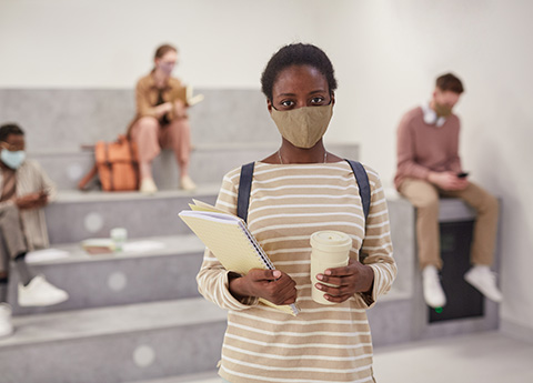 Student wearing mask, with school papers and coffee cup
