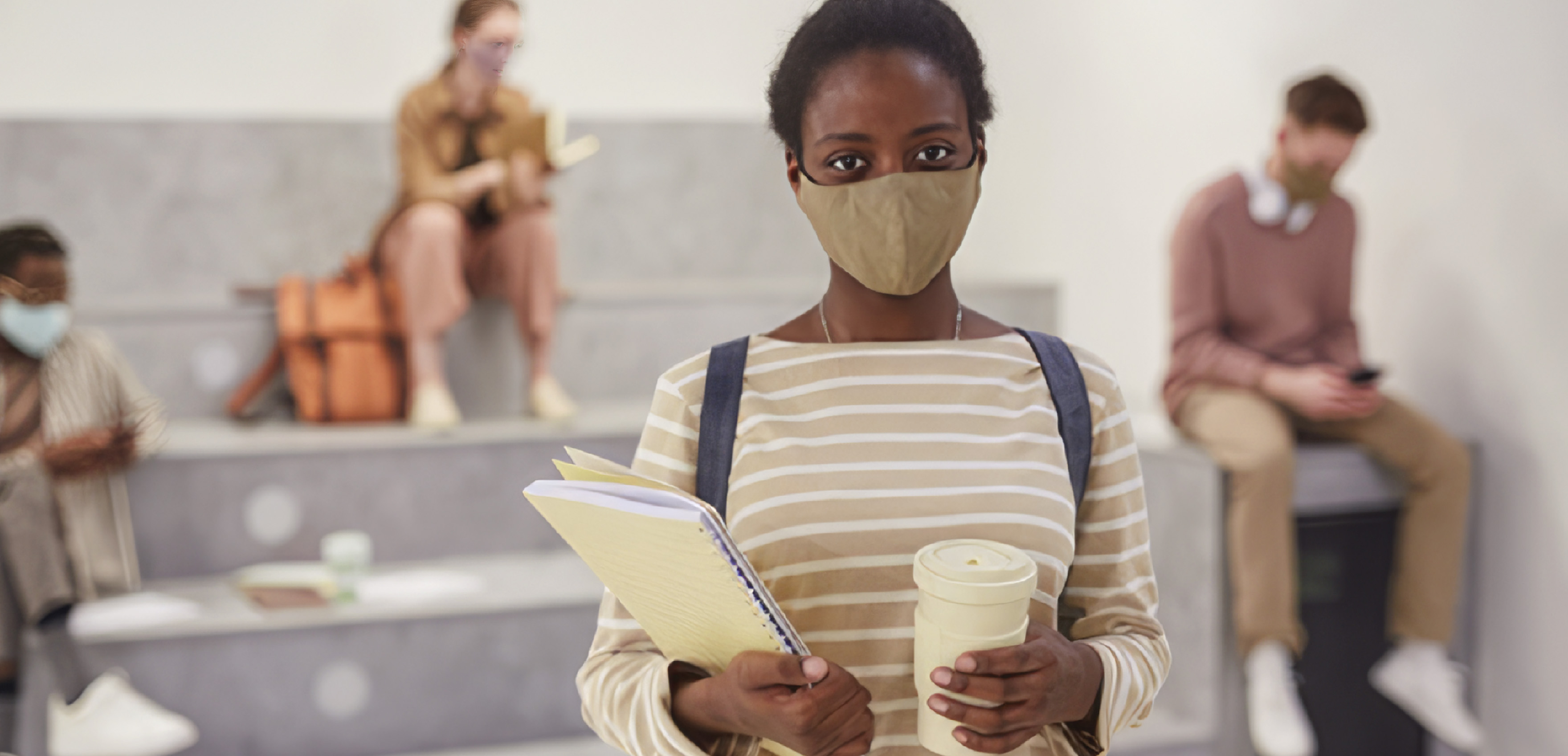 Student wearing mask, with school papers and coffee cup