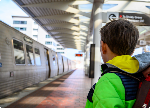 Passenger standing on a Washington, DC Metro platform as a train arrives, with covered station structure and platform extending into the distance