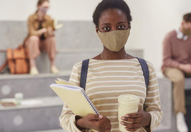 Student wearing mask, with school papers and coffee cup