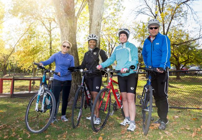 People holding their bicycles while standing in a park with trees in the background