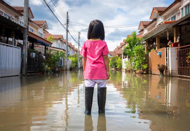 Young girl in standing water, facing flooded street. 