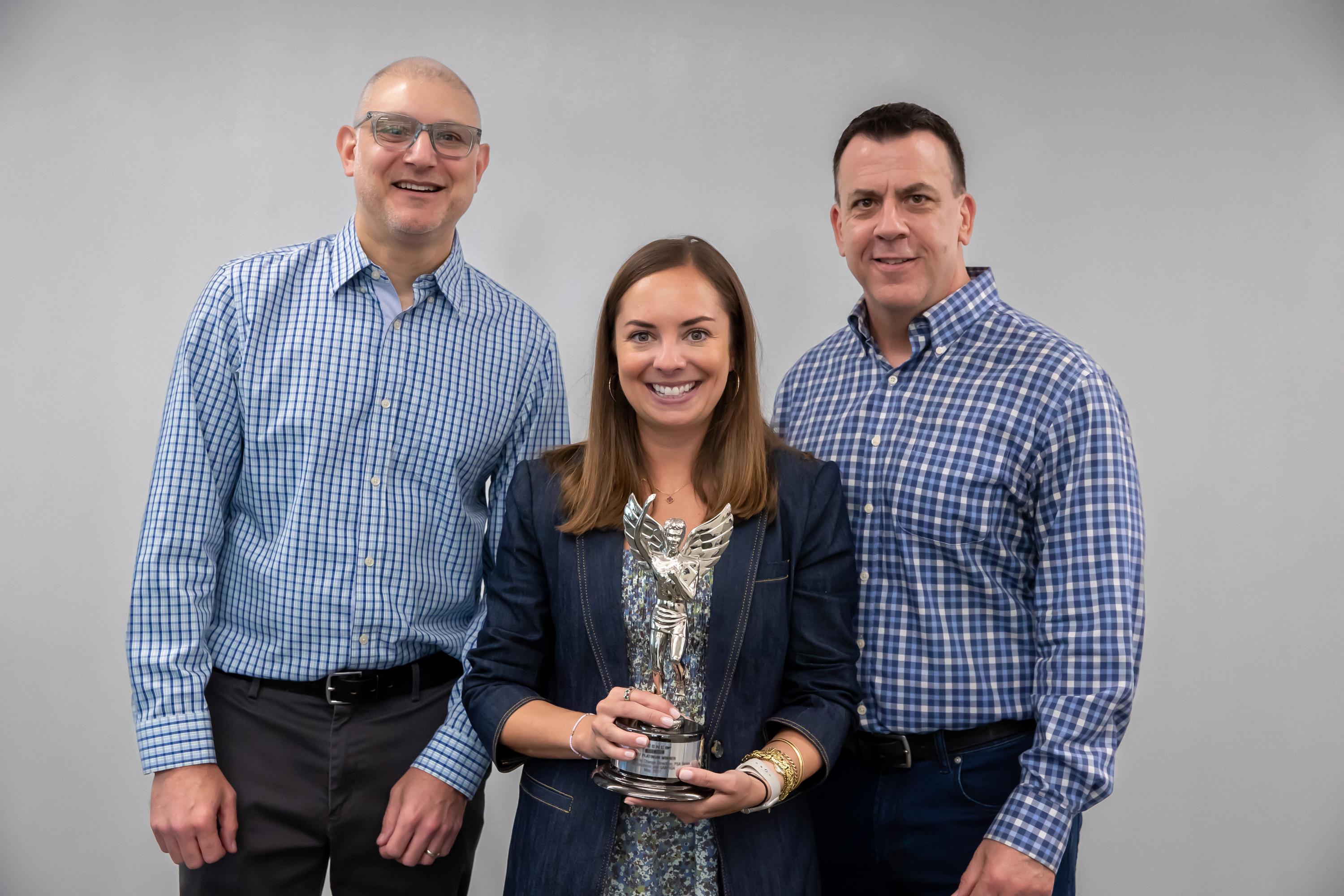 Three iq solutions team members holding an award and smiling