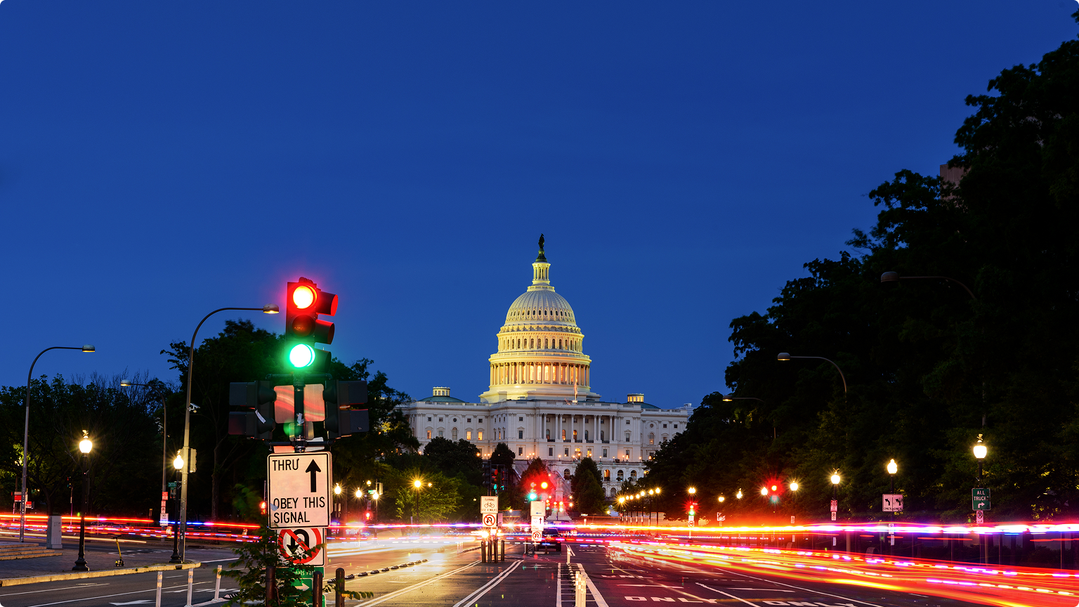 U.S. Capitol building at dusk with traffic light and long-exposure vehicle lights along a city street